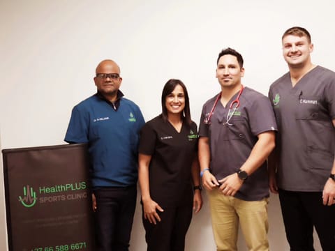 Four HealthPLUS clinicians in scrubs beside the HealthPLUS Sports Clinic banner; Dr Arthur Williams on the far left, with G. Van Wyk, Dr BD Haupt, and C Hamman